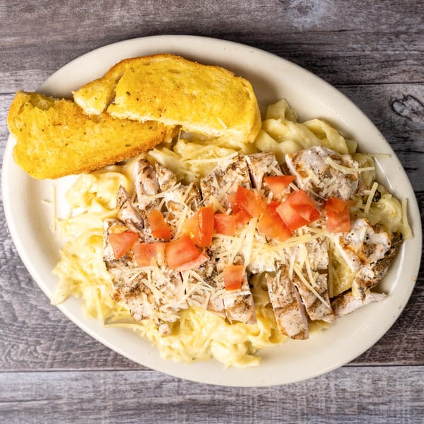Chicken alfredo pasta with diced tomatoes, shredded cheese, and two slices of garlic bread.
