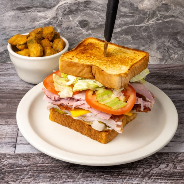 Club sandwich with toasted bread, ham, turkey, cheese, lettuce, tomato, and a side of fried okra.