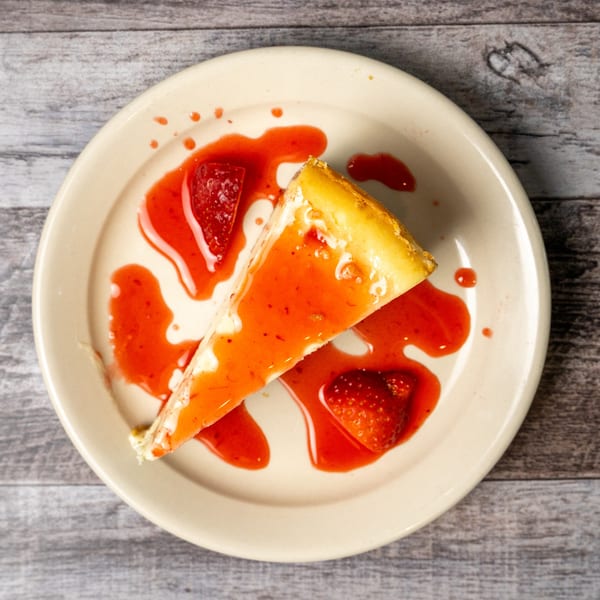 Slice of cheesecake drizzled with strawberry sauce and garnished with fresh strawberries on a plate.