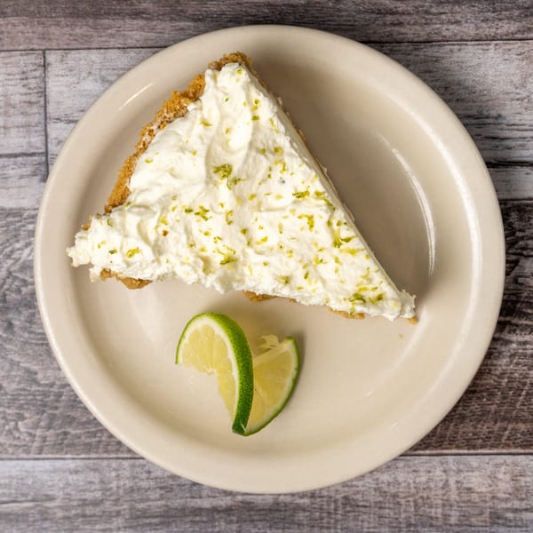 A slice of key lime pie with whipped cream and lime zest, garnished with two lime wedges.