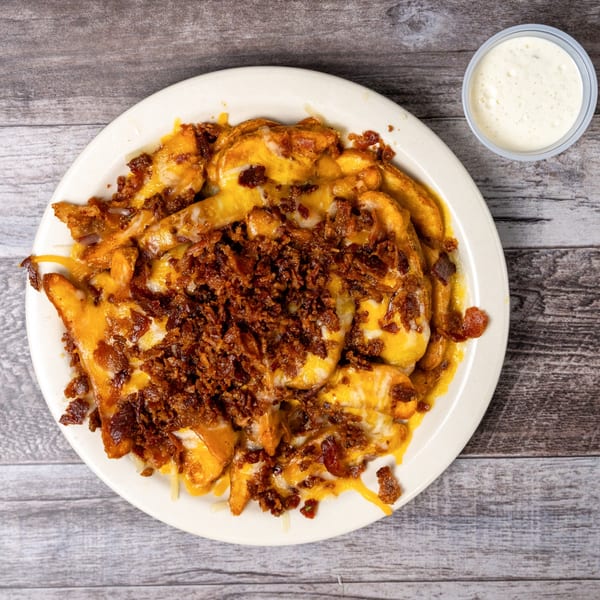 A plate of golden cheese fries topped with crispy bacon bits, with a side of ranch.