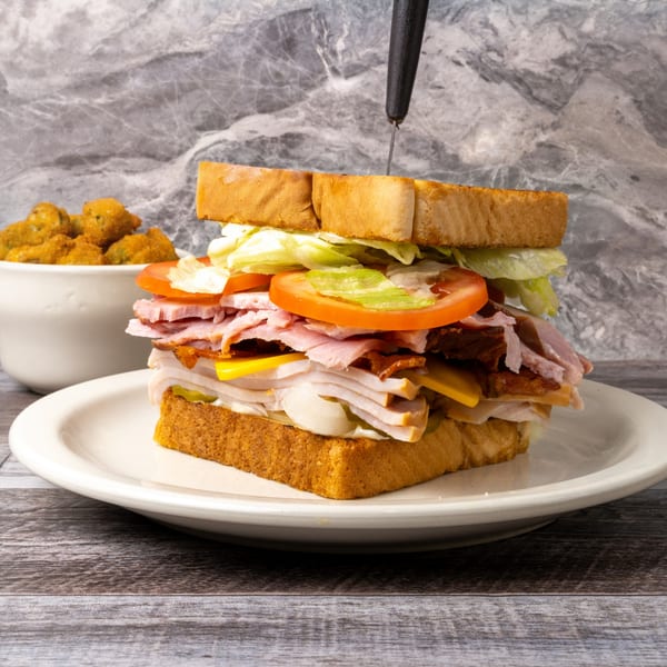 A large club sandwich with a knife, and a bowl of fried okra on a white plate.